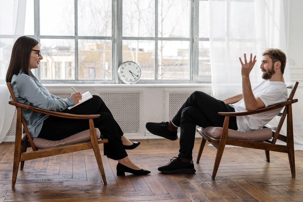 A man in counselling facing a counsellor in a bright drug rehab therapy room