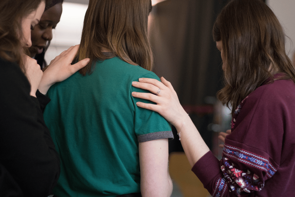 A group of young women holding their hands on one another's shoulders in a group rehab therapy session | Which Rehab