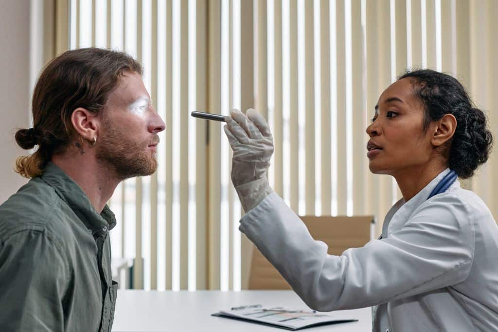 A man in an NHS drug service having his eyes inspected by a female doctor