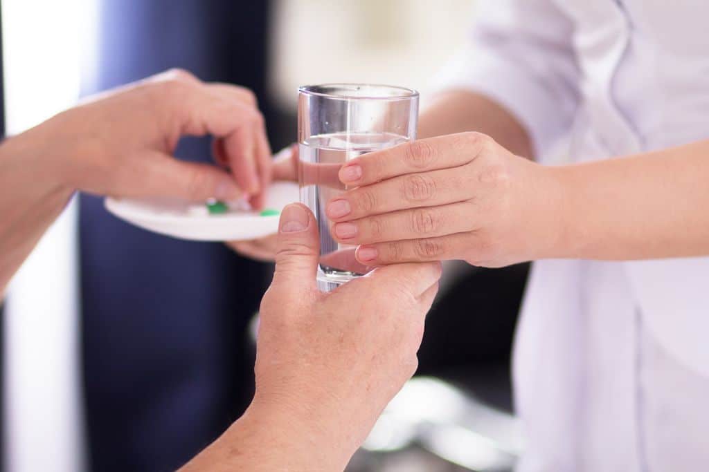 A close up of hands handing detox medication and a glass of water to a patient - Which Rehab