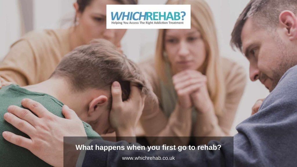 A group of people supporting a man with his head in his hands at a group addiction therapy session with the Which Rehab logo and blog title, what happens when you first go to rehab?
