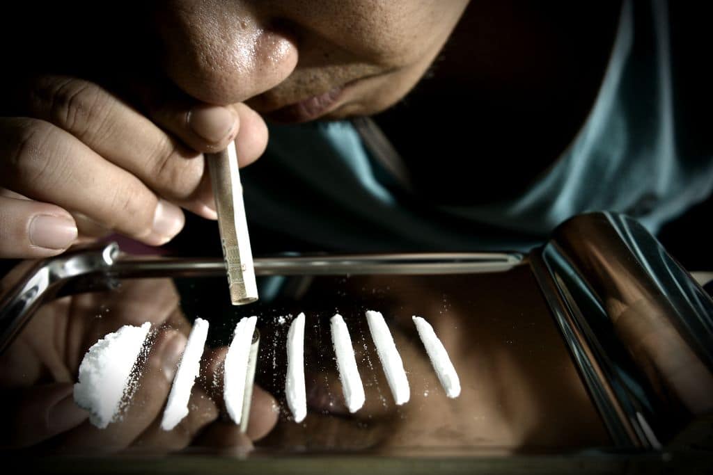 A man with a cocaine addiction snorting lines of coke with a rolled up paper note - Which Rehab