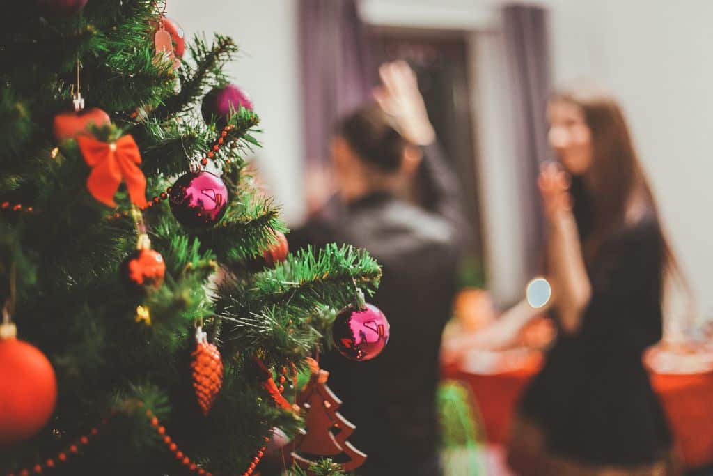 A close up of a Christmas tree with two people dancing in the background at a Christmas party - Which Rehab