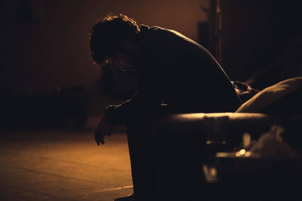 A depressed man sitting in the dark on a bench with his head down and his hands on his knees - Which Rehab
